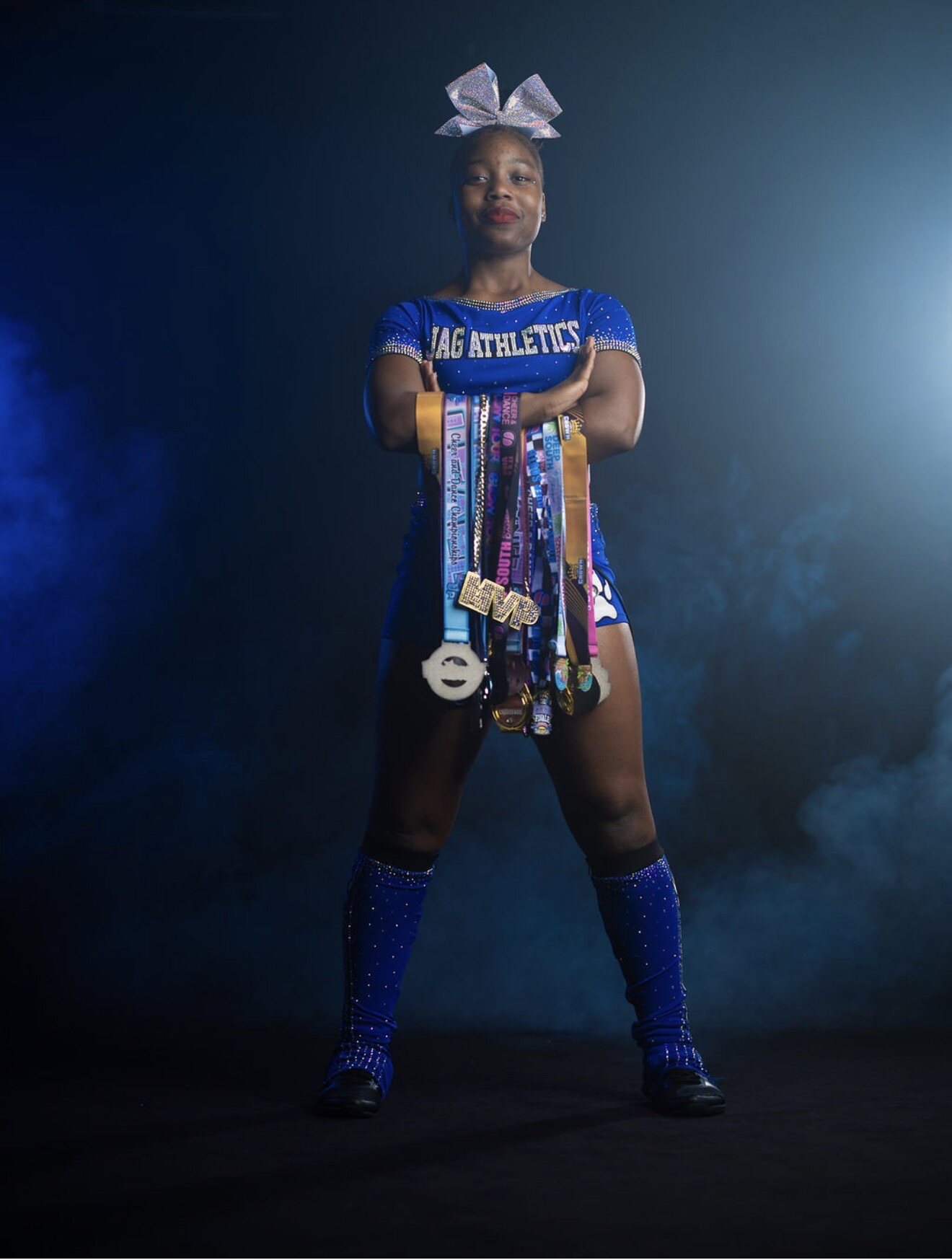 Cheer athlete wearing a royal blue JAG Athletics uniform and displaying competition medals