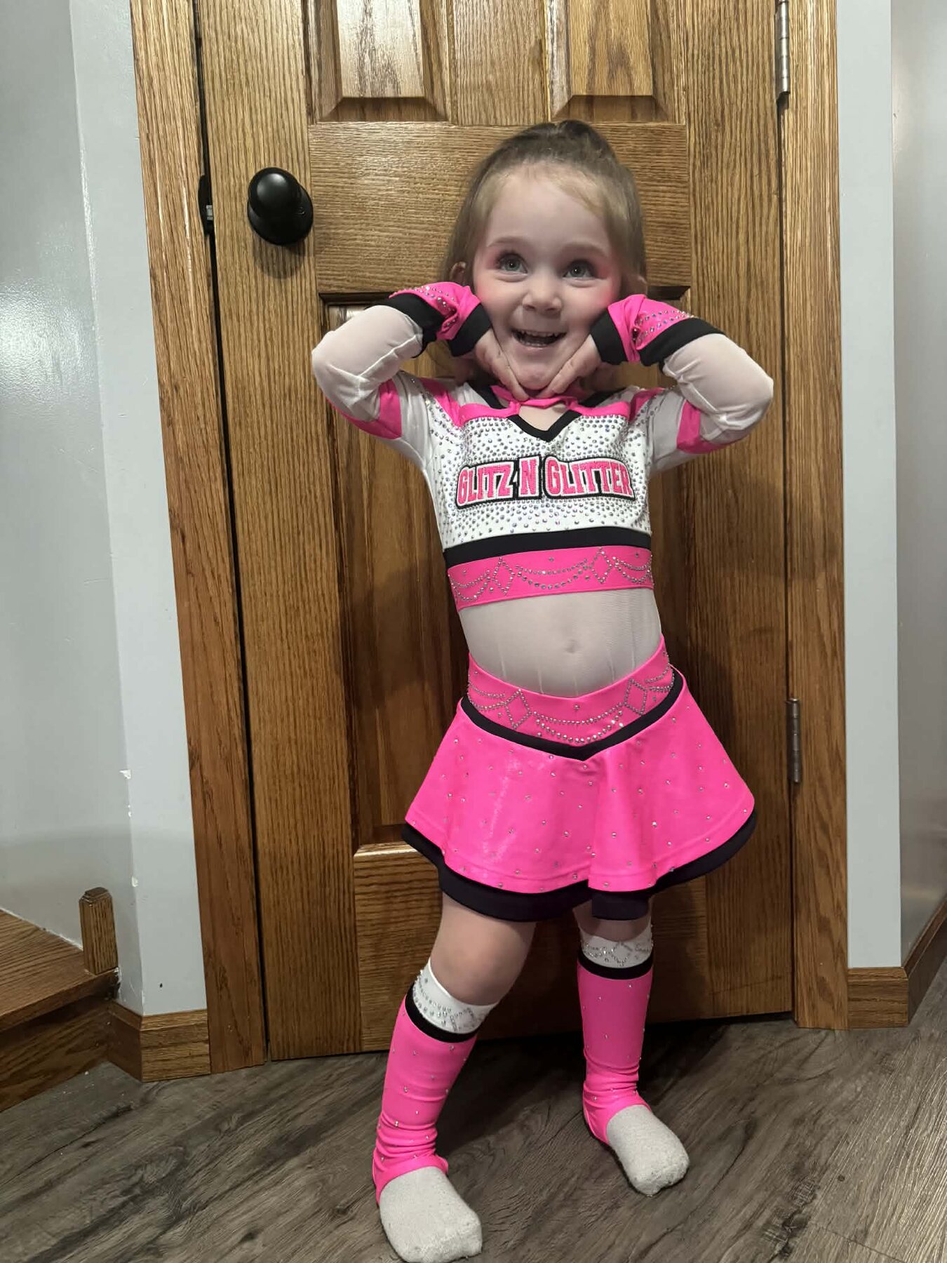 Young cheer athlete modeling the front of a hot pink, white, and black rhinestone uniform